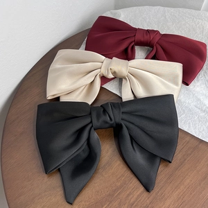 Detailed view of large satin bow hair clips in burgundy, champagne, and black silk