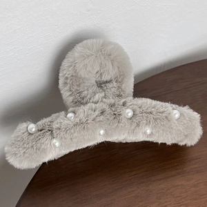 Close-up of a light grey plush hair claw clip decorated with white pearls on a wood table