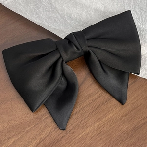 Detailed view of elegant black satin bow hair clip with smooth silk texture and flowing ribbon