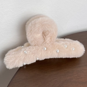 Detailed view of plush cream hair claw clip with white pearl accents on wooden surface