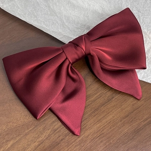 Close-up of elegant wine red satin bow hair clip with glossy silk texture and layered design