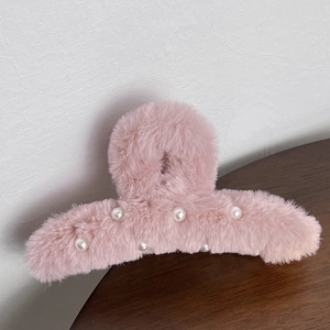 Close-up of pink plush shark hair claw clip with embedded pearls on a wooden surface