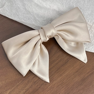 Detailed top view of large champagne satin bow hair clip on a vintage wooden surface