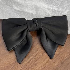Close-up of elegant black satin bow hair clip with a silky finish on wood surface