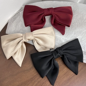 Close-up of triple-layered satin bow hair clips in burgundy, champagne, and black colors
