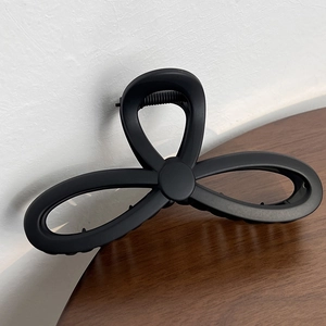 Detail of a large matte black hair claw clip with a minimalist bow design on a wooden surface
