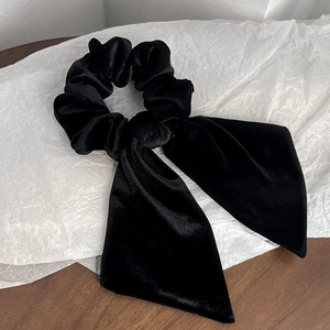 Detail view of black velvet bow scrunchie with long ribbons on white art paper
