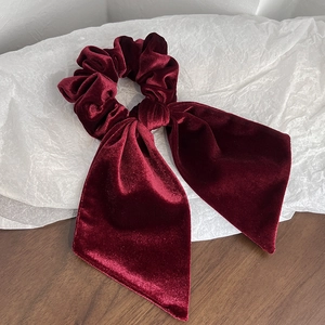 Detailed macro view of high-quality burgundy velvet hair scrunchie with long ribbon bow