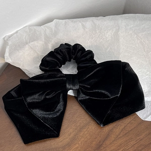 Detail of elegant black velvet hair scrunchie with oversized bow and silky texture