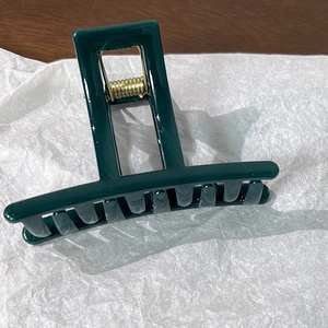 Detail of a dark green rectangular hair claw clip with a glossy finish and metal spring