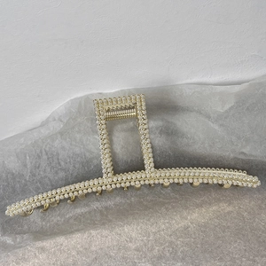 Vue détaillée d'une grande pince à cheveux dorée ornée de trois rangées de perles blanches