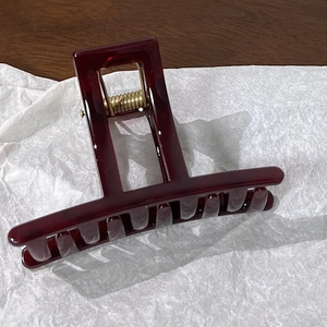 Close-up of translucent burgundy rectangular hair claw clip with golden metal spring