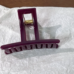 Macro detail of wine red jelly hair claw clip with golden metal spring on white background