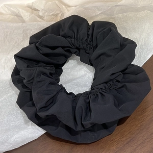 Detail of a large black pleated fabric scrunchie on a textured wooden background