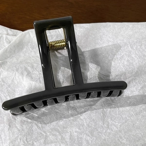 Detail of a sleek black rectangular hair claw clip with golden metal spring mechanism