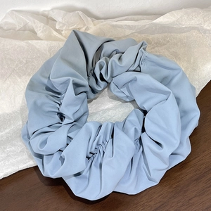 Detailed macro view of a misty blue pleated satin scrunchie on a wooden surface