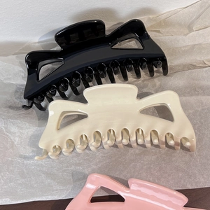 Three large elegant hair claws in black, cream and pink on a white textured background
