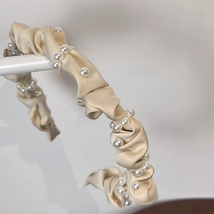 Nahaufnahme eines eleganten champagnerfarbenen Satin-Haarreifs mit weißen Perlen-Details