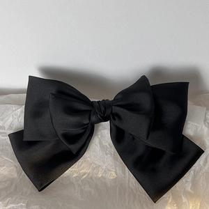 Detail of a large double-layer black satin bow hair clip with a smooth silky texture