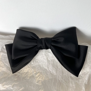 Detail of a large black vintage satin bow clip with multi-layered fabric and silk texture