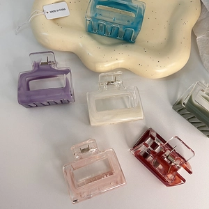 Detail of square acrylic hair claws in multiple colors on a white ceramic tray