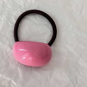 Dettaglio dell'ornamento in resina rosa e dell'elastico per capelli nero su carta bianca