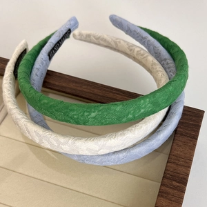 Three handmade jacquard fabric headbands in green, white, and blue on a wooden stand