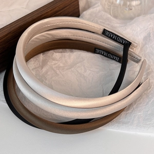 Detailed view of padded solid color headbands in beige, brown and black with satin finish