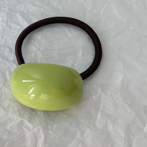 Dettaglio dell'elastico per capelli in resina verde chiaro a forma di fagiolo su carta