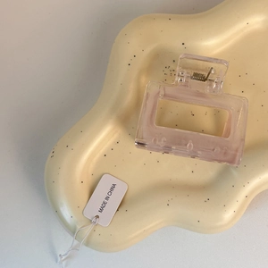 Detail of a square light pink translucent hair claw clip on a stylish wavy tray