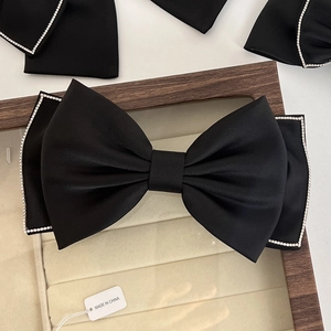 Close-up of black satin bow hair clip with sparkling rhinestones on a display box