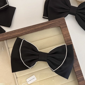 Macro detail of a black bow hair clip with rhinestones on a beige velvet tray