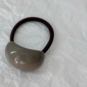 Dettaglio di una perla in resina grigia su un elastico per capelli marrone scuro elastico