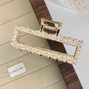Detail view of large gold hair claw clip with elegant faux pearls on a display tray