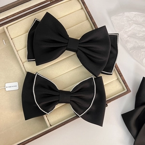 Detail of black bow hair clip with rhinestones and matte satin on a beige velvet box