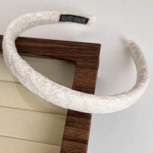 Detail view of handmade cream lace headband with wave pattern and woven brand label