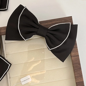Close-up of black satin bow hair clip with sparkling rhinestone edges in a velvet box