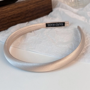 Detailed close-up of champagne satin headband with handmade woven label on fabric texture