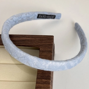 Close-up of light blue lace headband with handmade label on wooden display stand