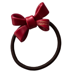 Polished red acrylic bow hair tie with black elastic band and gold handmade lettering