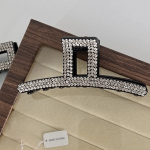 Detailed close-up of a black hair claw clip with rhinestones on a beige velvet display
