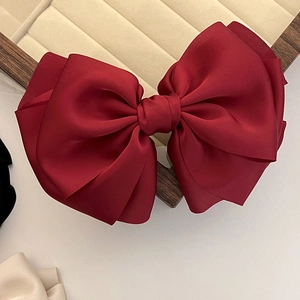 Macro shot of large burgundy satin bow hair clip on a premium velvet jewelry display tray