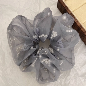 Detail van een grote grijze organza scrunchie met witte parels op papieren achtergrond