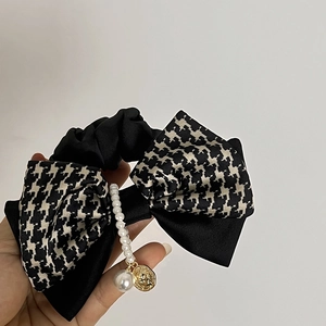 Détail d'un chouchou élégant avec motif pied-de-poule, perles et breloque en pièce dorée