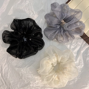 Detailoverzicht van drie transparante organza scrunchies met parels in zwart, blauw en crème
