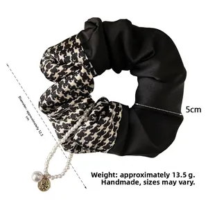 Detailed view of black satin scrunchie with houndstooth pattern and pearl chain pendant