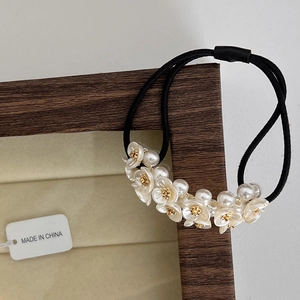 Détail de chouchou floral avec fleurs en résine blanche et perles sur élastique noir