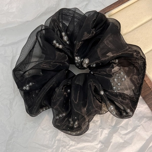 Detailopname van een elegante zwarte tule scrunchie met grijze parels op een display