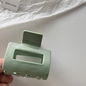 Detaillierte Nahaufnahme einer mintgrünen quadratischen Haarklammer in der Hand