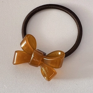 Macro detail of amber resin bow hair tie with golden handmade lettering and elastic band